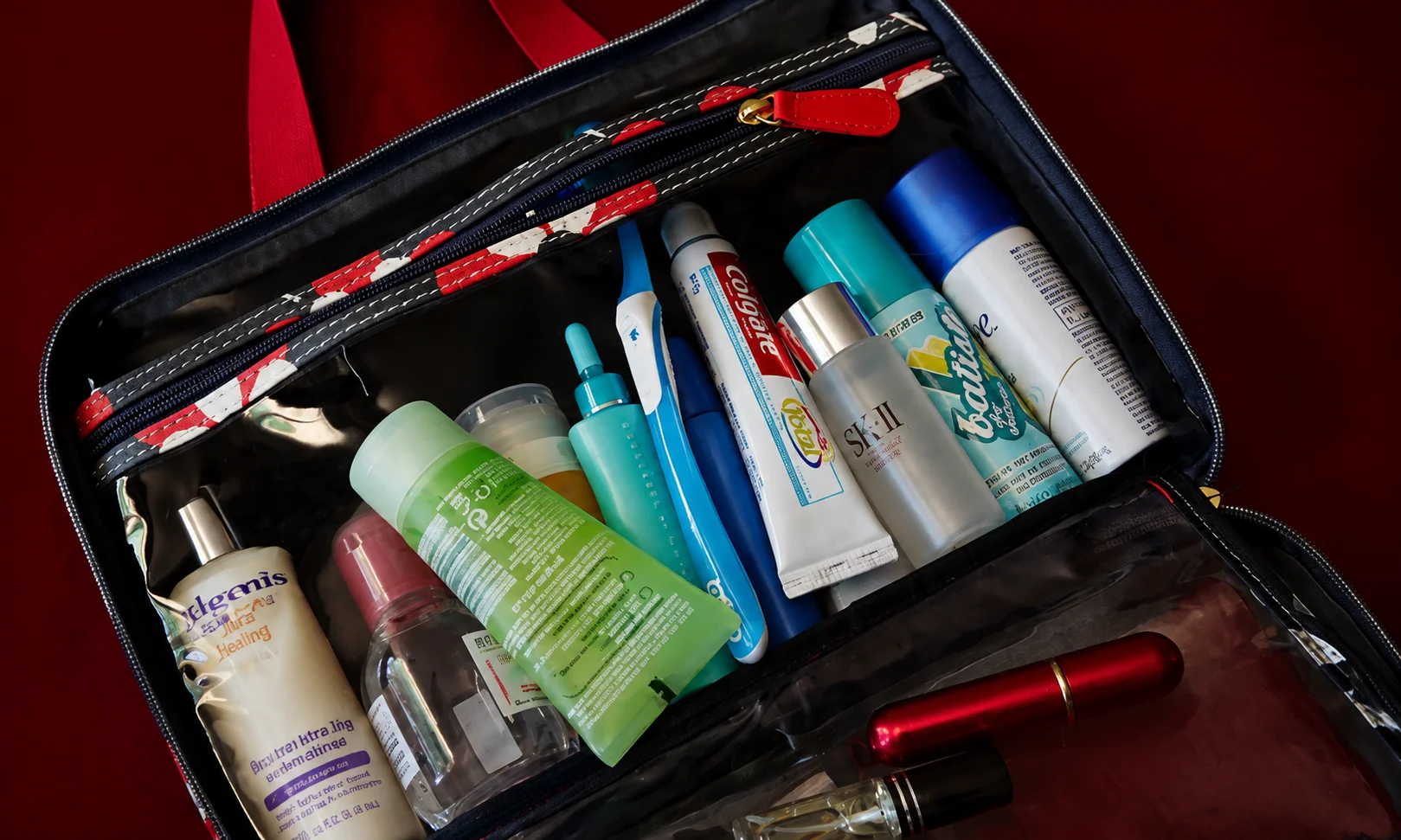 A toiletry bag filled with travel bottles and accessories showcased under a warm red-toned aesthetic.