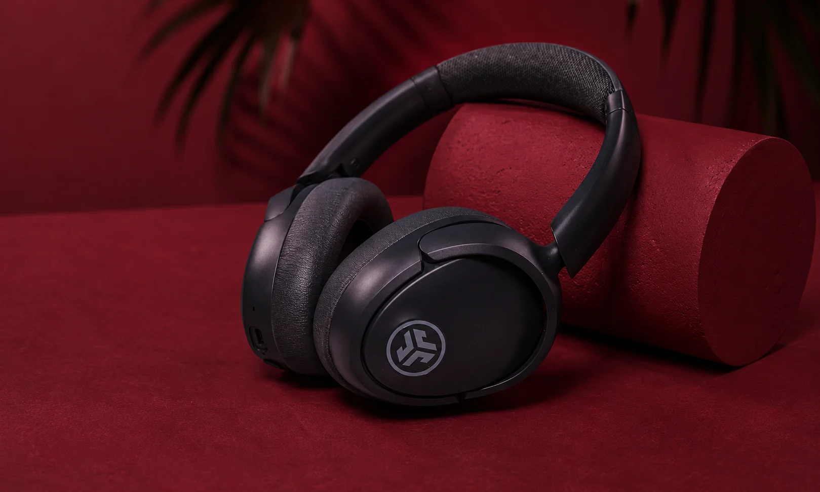 JLab JBuds Lux ANC over-ear headphones resting on a red surface.