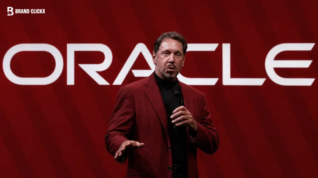 Larry Ellison speaking on stage in front of a giant Oracle logo against a dark red background