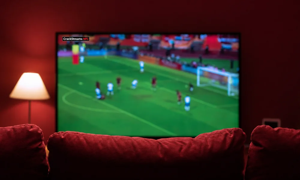 A television screen broadcasting a live football game in a dark room set against a red aesthetic.