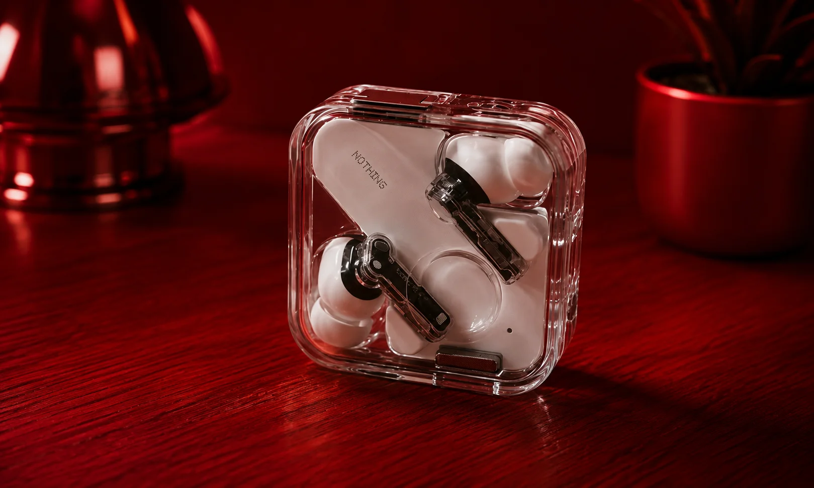 Nothing Ear transparent earbuds displayed on a dark red platform.