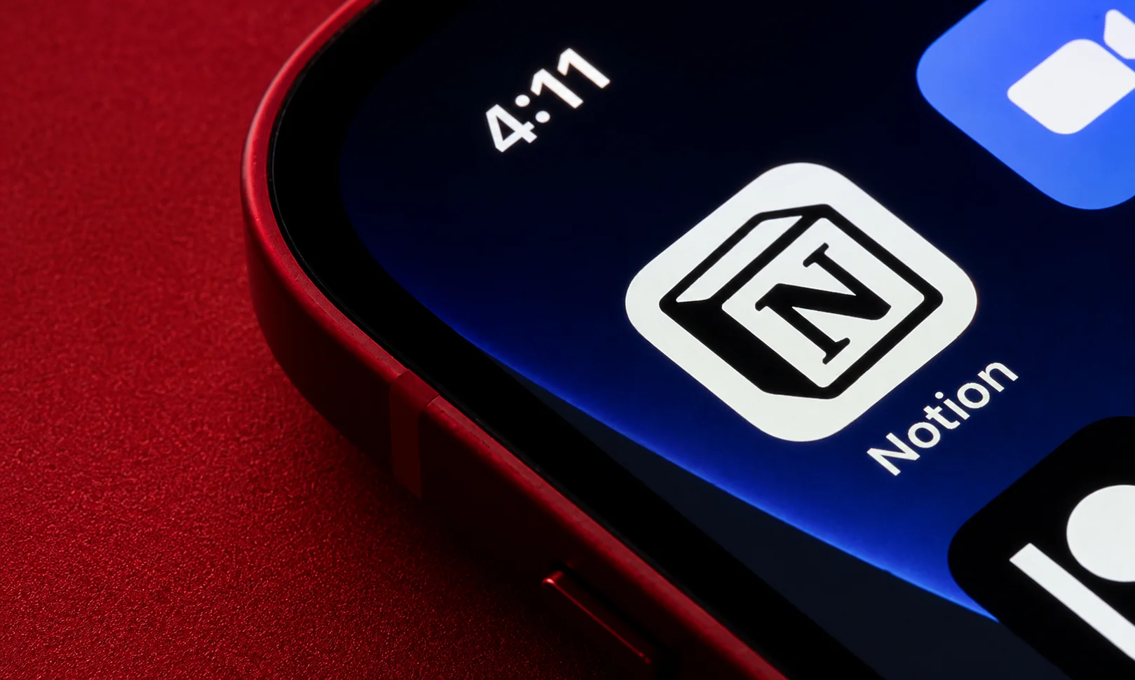 Close-up of a smartphone screen showing the Notion app next to a red desk setup