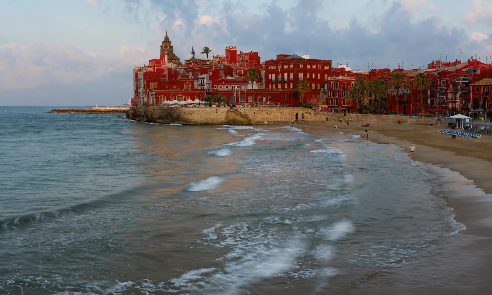 Sant Sebastian beach in Sitges with the historic Sant Bartomeu and Santa Tecla church visible on the coastline.