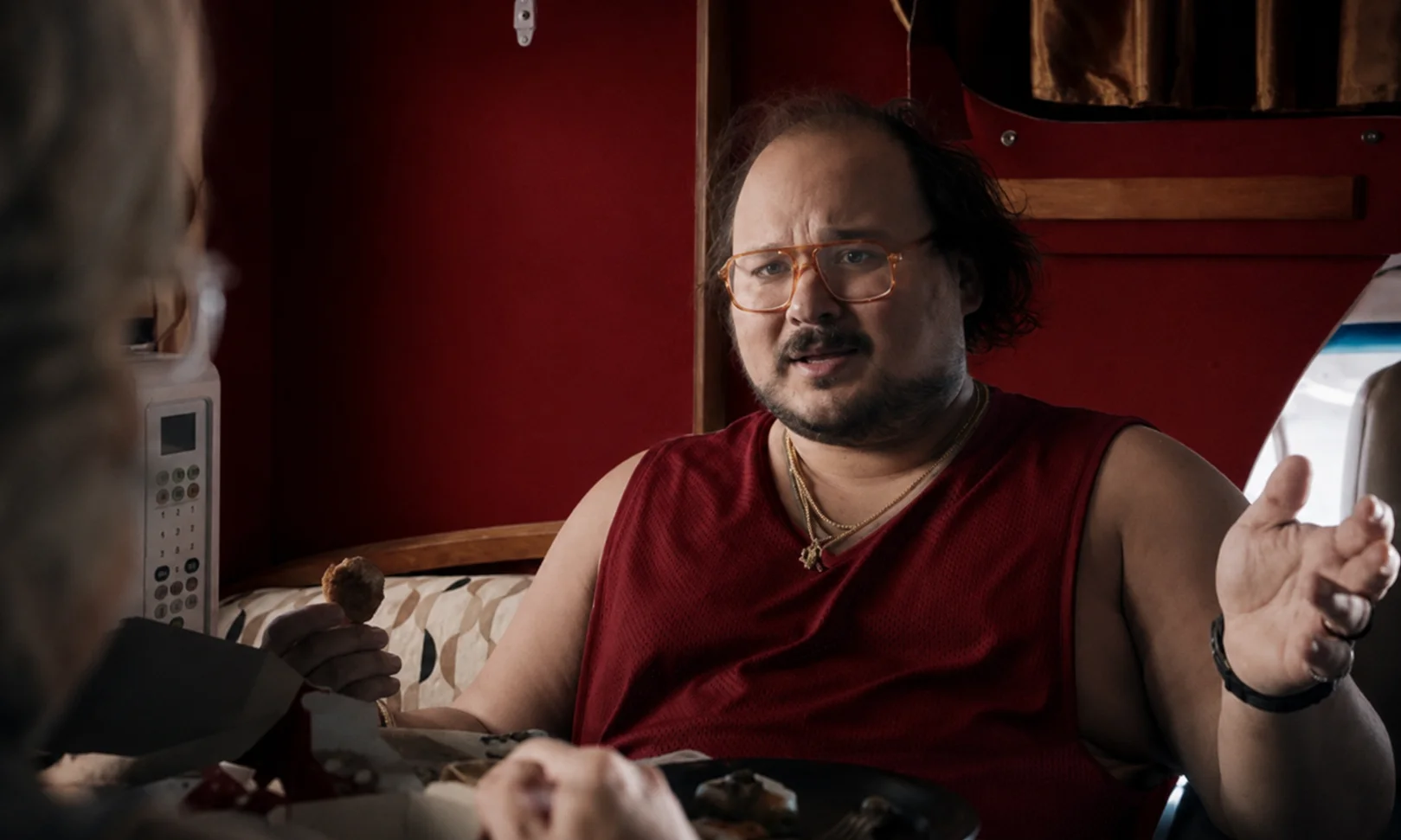 Portrait of Stavros Halkias as Dave set against a rich red studio backdrop.