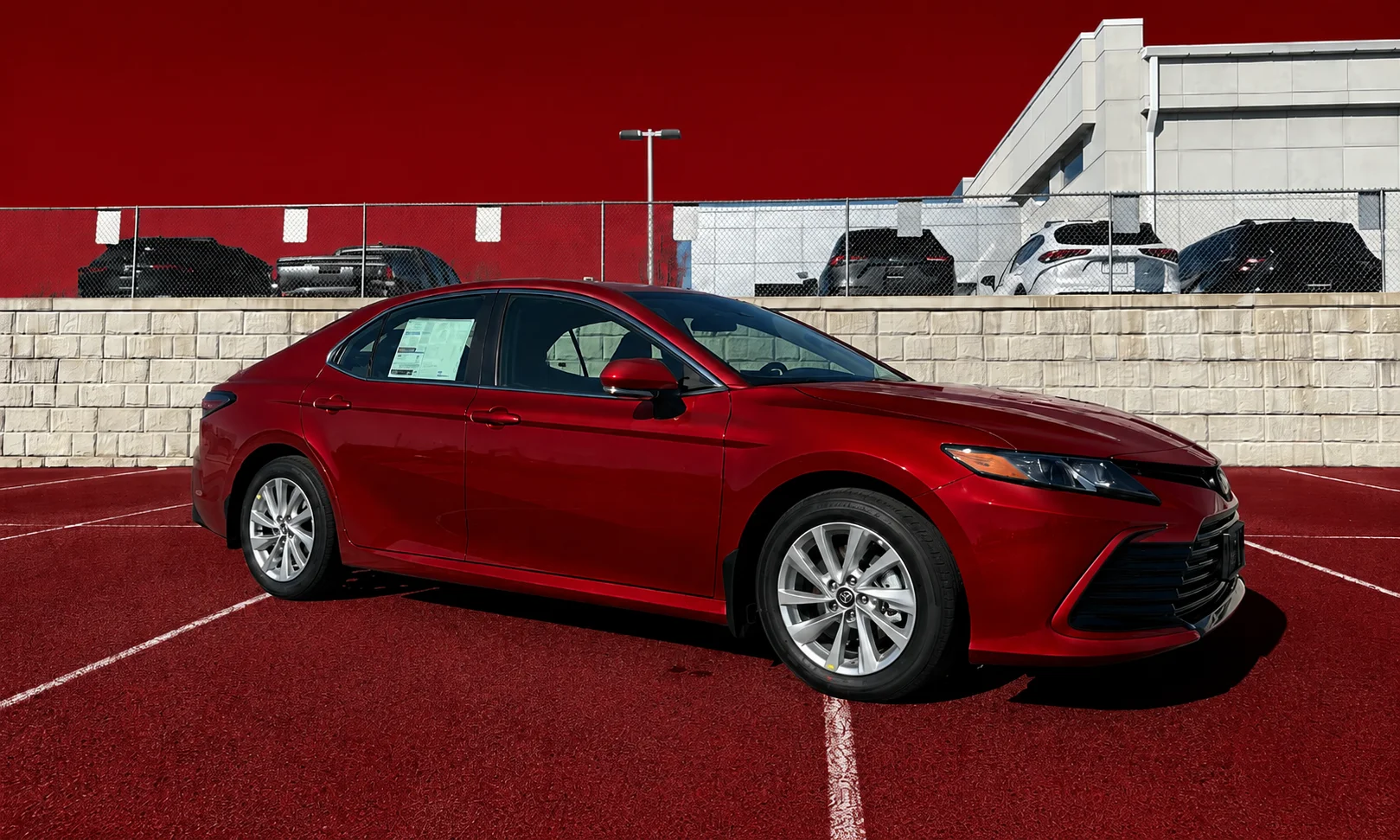 | Toyota Camry Trims 2026: Which One Is Best? Toyota Camry LE sedan parked in a showroom with a dark red backdrop
