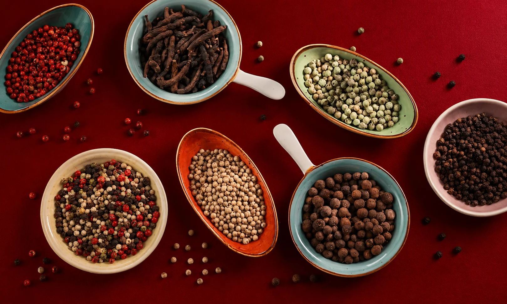 Four small bowls displaying black, white, green, and red peppercorns side-by-side.
