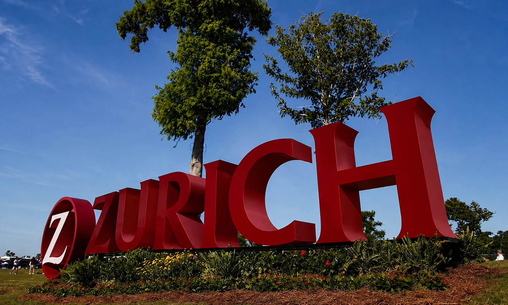 | Best Insurance Companies in the World in 2026 Large red 3D lettering displaying the Zurich brand sign against a clear blue sky and green trees.