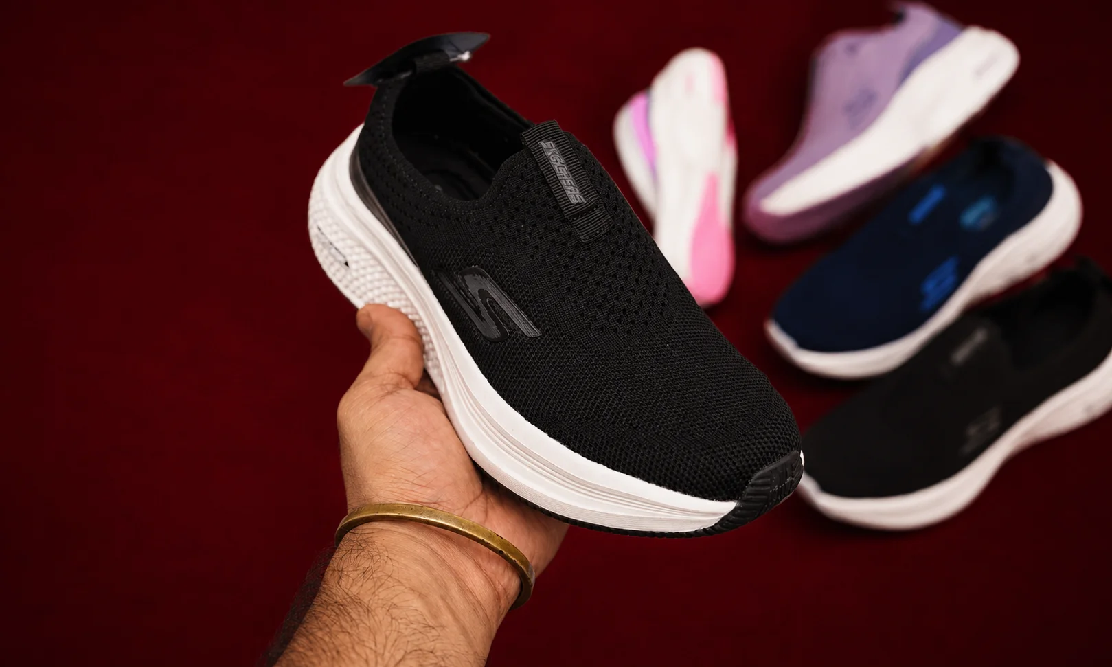 Hand holding a black Skechers shoe against red velvet