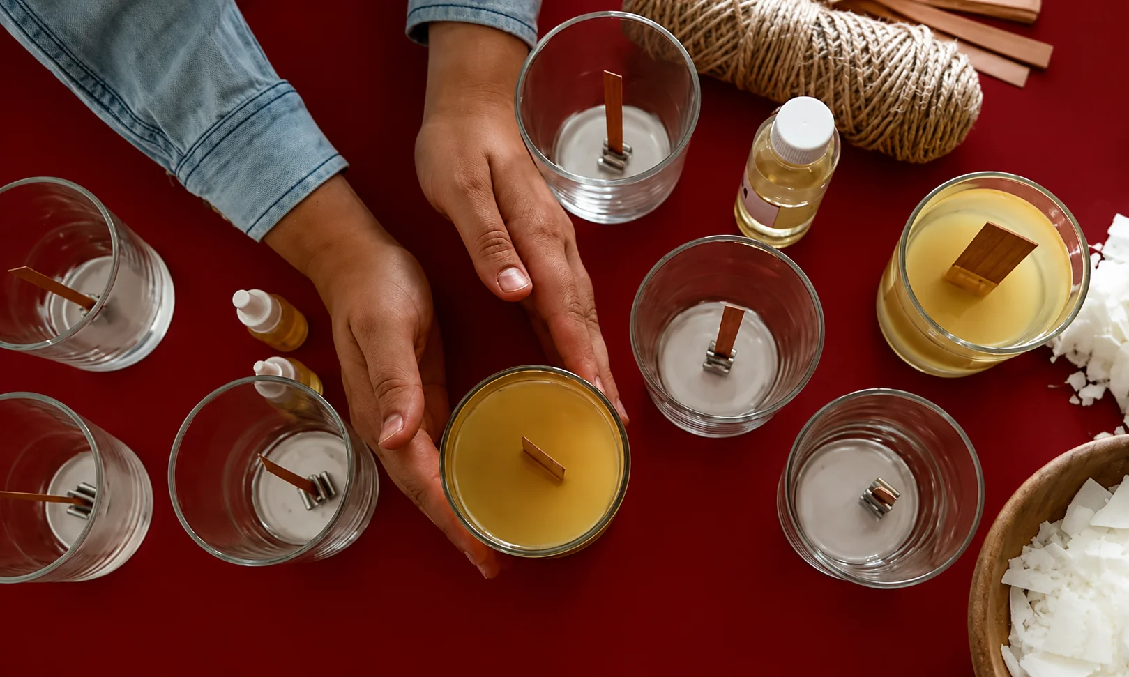 Hands pouring warm wax into molds for candle making on a red-themed table setup