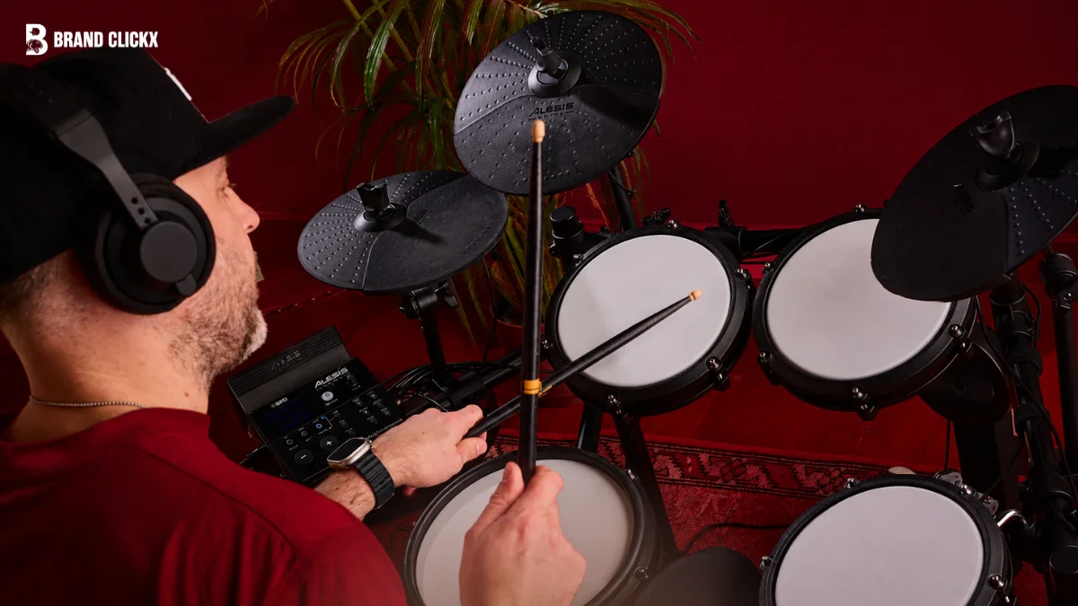 A drummer wearing headphones playing an electronic drum kit in a home studio setting