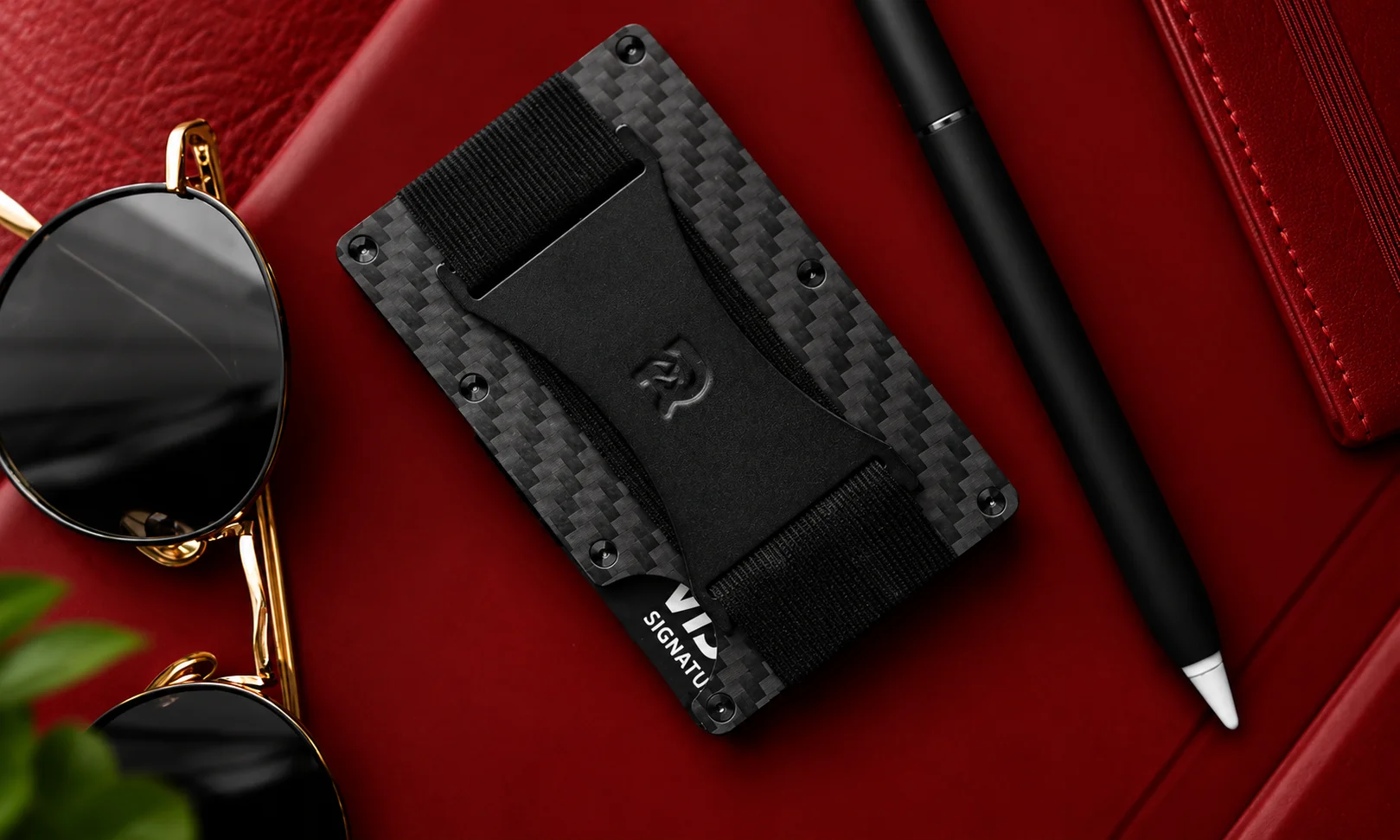 The Ridge Wallet 2.0 minimalist metal cardholder with a cash strap displayed next to sunglasses and a pen.